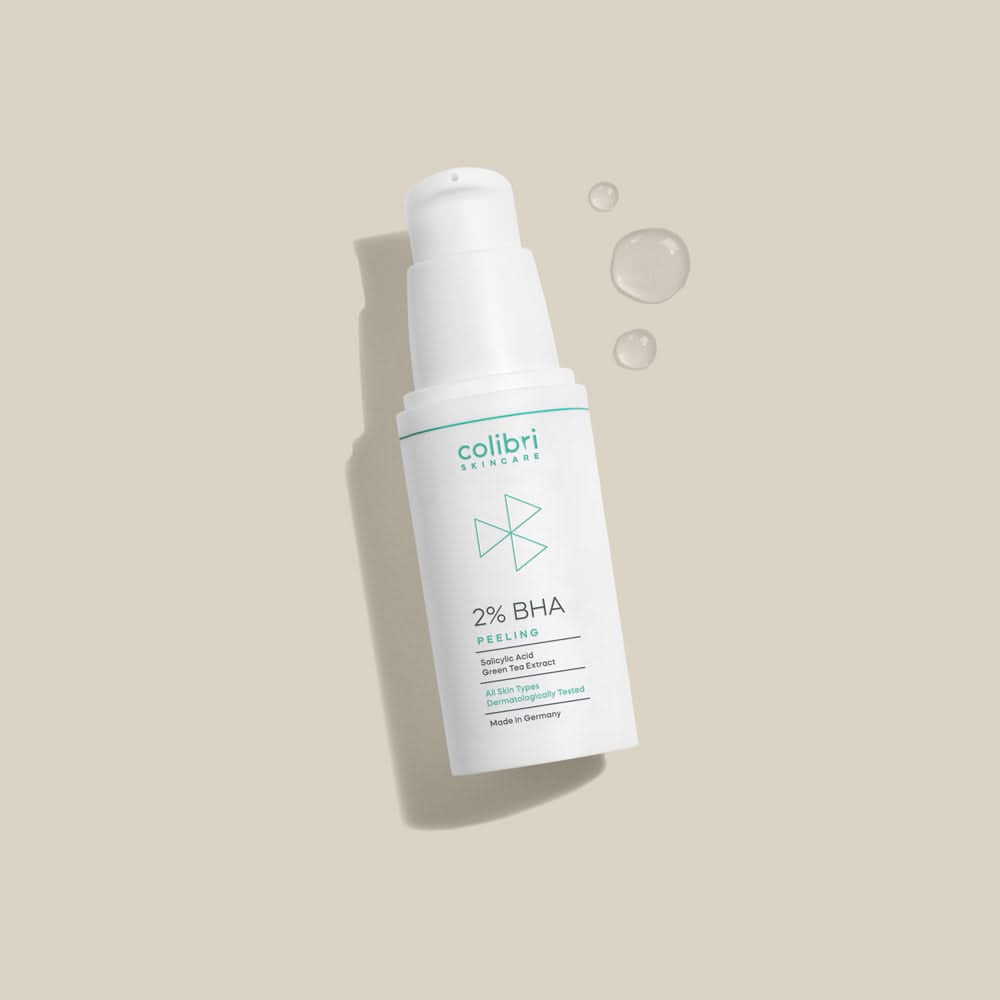 Weiße Flasche mit 2% BHA Peeling von Colibri Skincare auf beigem Hintergrund, daneben Flüssigkeitstropfen.