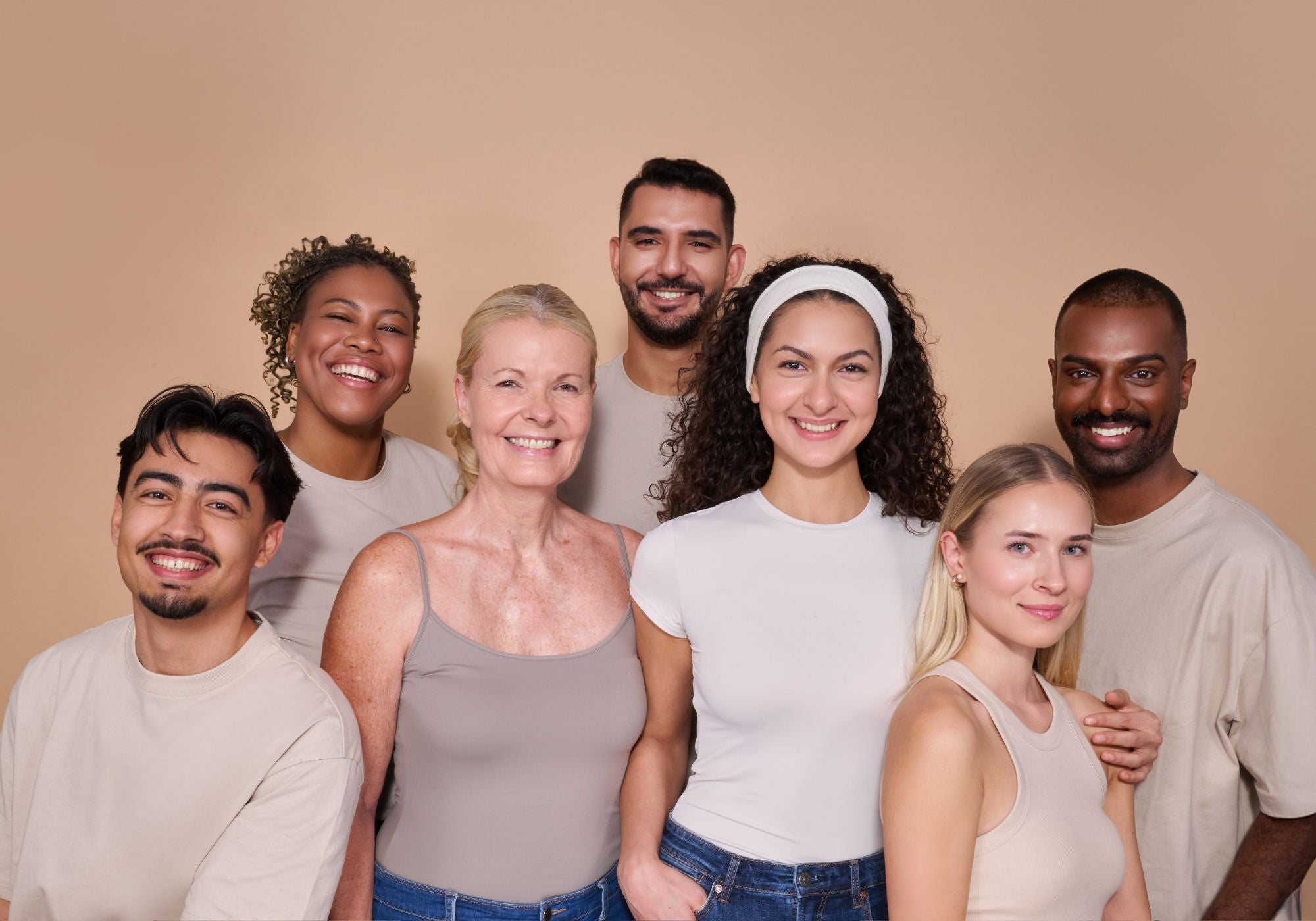 Gruppe von sieben lächelnden Personen in beigen Oberteilen vor einem neutralen Hintergrund.