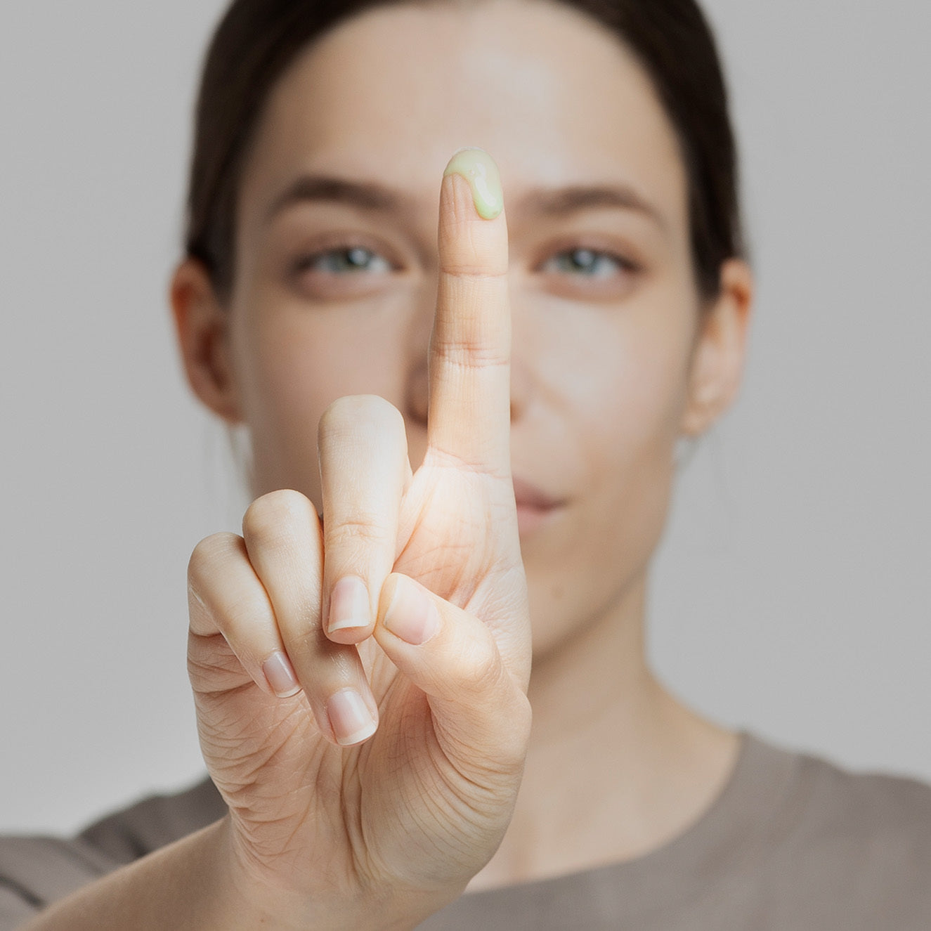 Eine Person zeigt ihren Zeigefinger mit einem grünen Cremefleck darauf nach vorne.