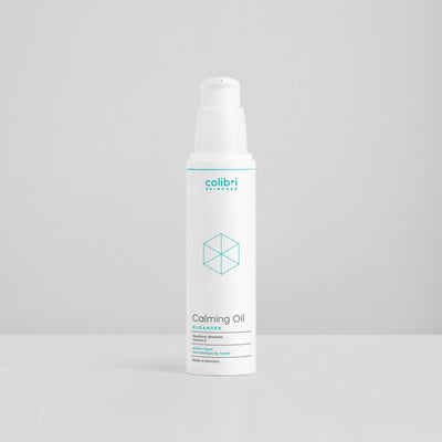 Weiße Flasche mit der Aufschrift "Colibri Skincare, Calming Oil Cleanser" vor grauem Hintergrund.