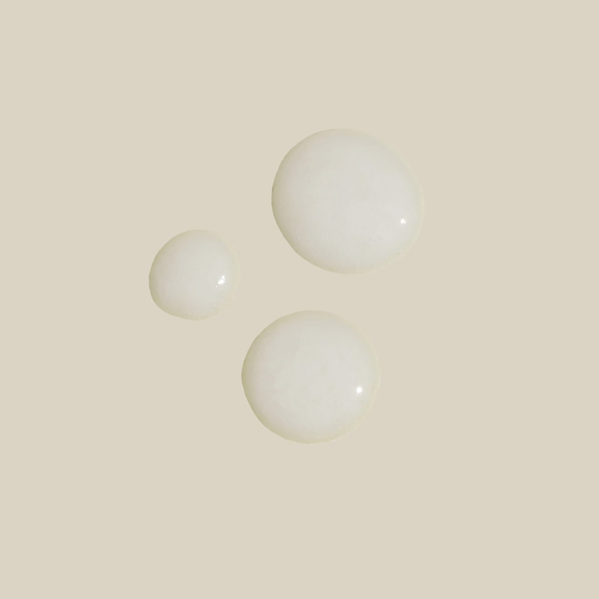 Drei weiße Flüssigkeitstropfen auf beigem Hintergrund.
