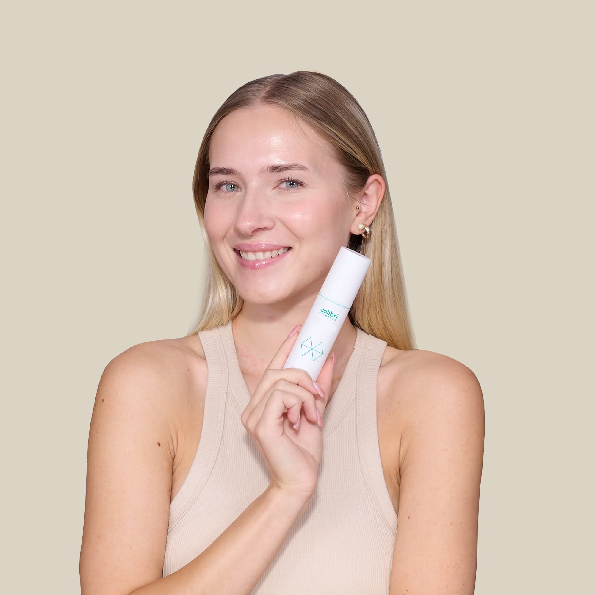 Eine Frau hält eine weiße Flasche mit grünem Logo, lächelt und trägt ein beige Tanktop vor einem hellen Hintergrund.