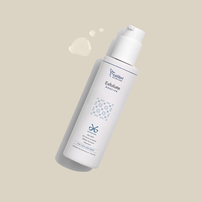 Weiße Flasche eines Exfoliate Boosters auf beigem Hintergrund mit einigen Tropfen daneben.