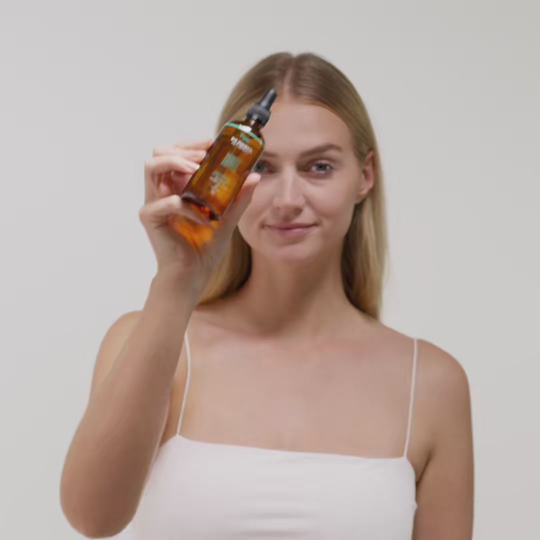 Frau mit langen Haaren zeigt eine bernsteinfarbene Flasche mit Pipette in Richtung Kamera.