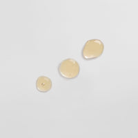 Drei beige Flüssigkeitstropfen auf einer hellen, glatten Oberfläche.